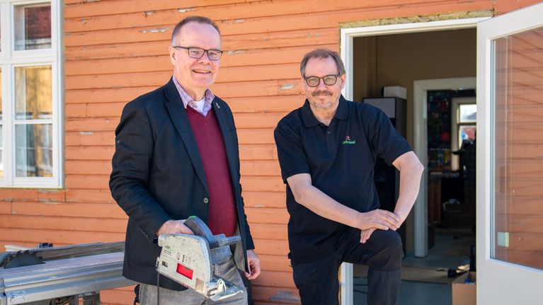 Pasi Vainio ja Mikko Vartiainen seisovat vielä rakenteilla olevalla terassilla. Taustalla näkyy Vinhan kirjakaupan oranssi lautaseinä. Vainiolla on kädessään höylä.