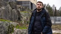 Mies seisoo kivien edessä ulkona pukeutuneena siniseen toppatakkiin.