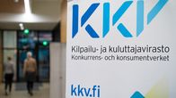 En närbild på en skylt med texten KKV, Konkurrens- och konsumentverket. I bakgrunden syns en människa som går längs KKV:s korridorer.