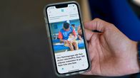 En hand håller upp en mobiltelefon med den svenskspråkiga startvyn för Yle-appen. Skärmen visar en nyhet om att över 100 miljoner människor i världen är på flykt.