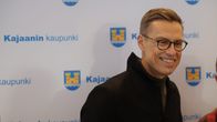 Tasavallan presidentti Alexander Stubb hymyilee, taustalla lakana, jossa on Kajaanin kaupungin logoja.