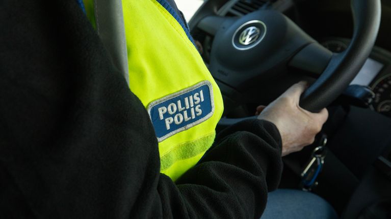 En person med reflexväst med texten "POLIISI POLIS" kör en bil.