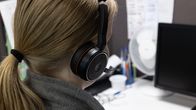 En kvinna sitter framför en dator. På sig har hon ett headset.