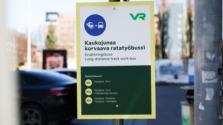Tampereen rautatieasemalla tolpassa kyltti, jossa teksti "kaukojunaa korvaava ratatyöbussi" ja kolmen reitin bussien numerot.