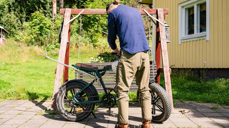 En man underhåller en elcykeln på en gård vid ett gult hus.
