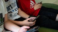 Tre små pojkar sitter och skrollar på sina smart telefoner. 