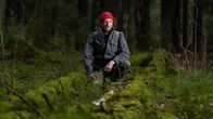 Luontokartoittaja ja metsäaktivisti Olli Manninen maassa makaavan, lähes sammaleen peittämän lahopuun vieressä Pirunkorven alueen Ruotsinkylän tutkimusmetsässä, Tuusula, 6.11.2023.
