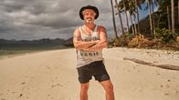 Nabaz Baki står med armarna i kors på en strand med palmer i bakgrunden.