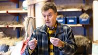 En person står i ett rum fyllt med hantverksmaterial och håller något i händerna, kanske relaterat till ett projekt eller en aktivitet.