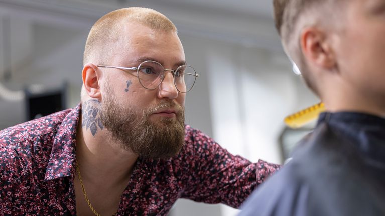 Parturi keskittyneenä leikkaamaan nuoren miehen hiuksia.