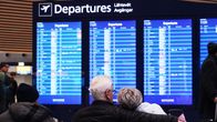 Människor sitter på Helsingfors-Vanda flygplats framför en avgångar-tavla.