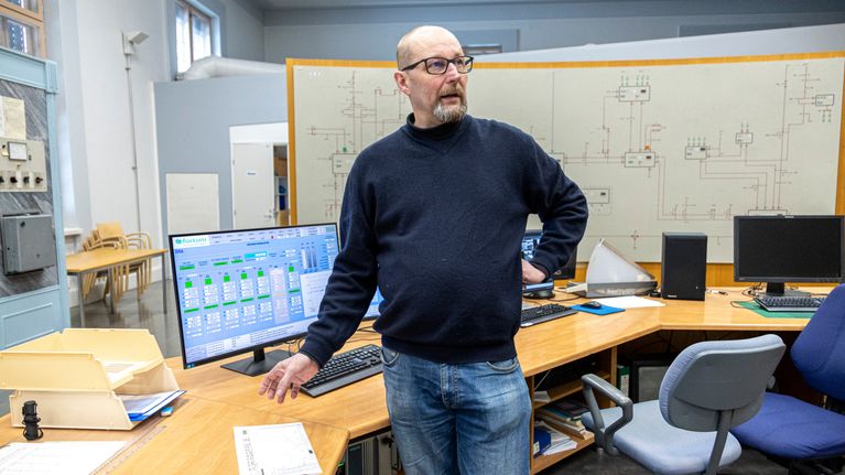 Erkki Luukkonen seisoo Imatran vesivoimalaitoksen valvomossa näyttöpäätteiden edessä.