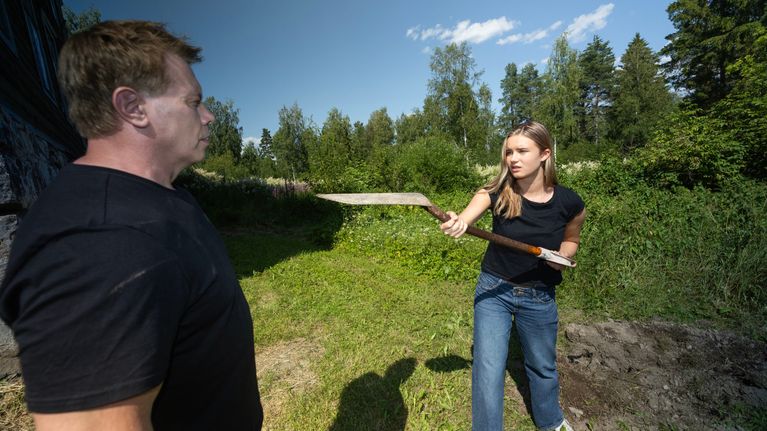 Nainen osoittaa lapiolla miestä.
