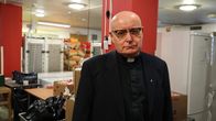 En skallig man med allvarlig uppsyn iklädd svart prästskjorta och mörk kavaj.