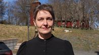 En kvinna med kort mörkt hår. I bakgrunden syns en röd träkyrka.