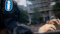 Anonyymi poliisi istuu tietokoneen edessä kuvattuna lasin läpi.