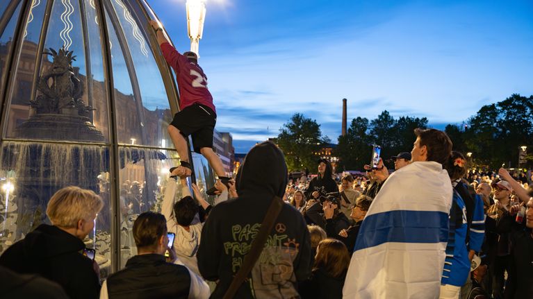 Ihmisiä seuraamassa, kuinka mieshenkilö yrittää kiivetä Keskustorin suihkulähteen kuvun päälle.