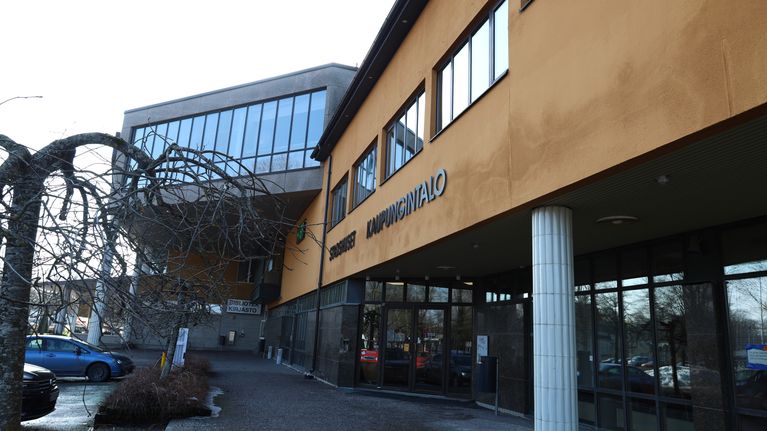 Pargas stadshus. En stenbyggnad i gult med en pelare bredvid entrén. Byggnaden har också områden som har stora fönster.