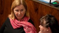 Två kvinnor i riksdagens ministerbås. Den som är i fokus är mörkblond och har en rosa scarf om halsen.