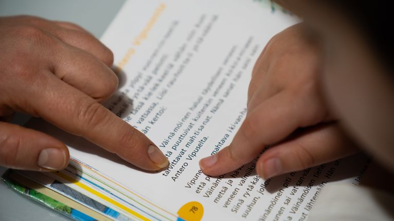 Toisen luokan äidinkielen kirjasta osoitetaan sormella mitä luetaan.