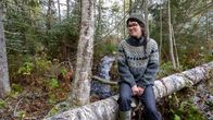 Väitöskirjatutkija Veera Saari istuu suojellun puron varrella kaatuneen puunrungon päällä.