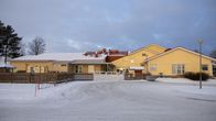 Helsingby skola är en ljusgul skolbyggnad här fotograferad på vintern med snö på marken. Det är ett grått, molnigt väder.