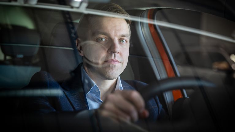Kalle Kaura istuu autossa kuljettajan paikalla.