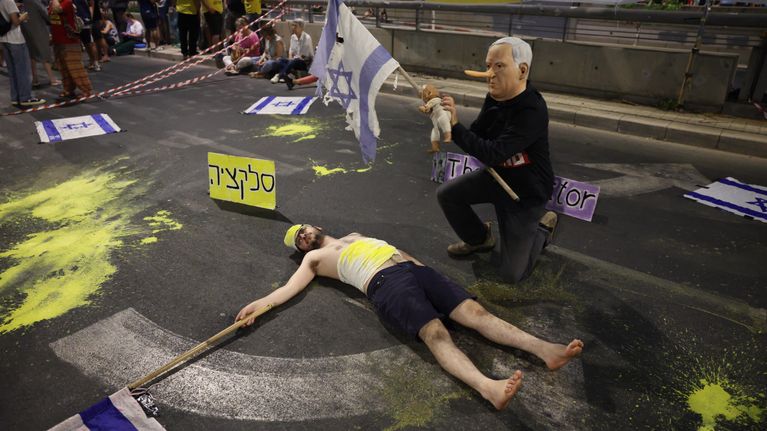 Kadulla mies makaa maassa Israelin lippu kädessään, toinen henkilö polvillaan vieressä naamio kasvoillaan.