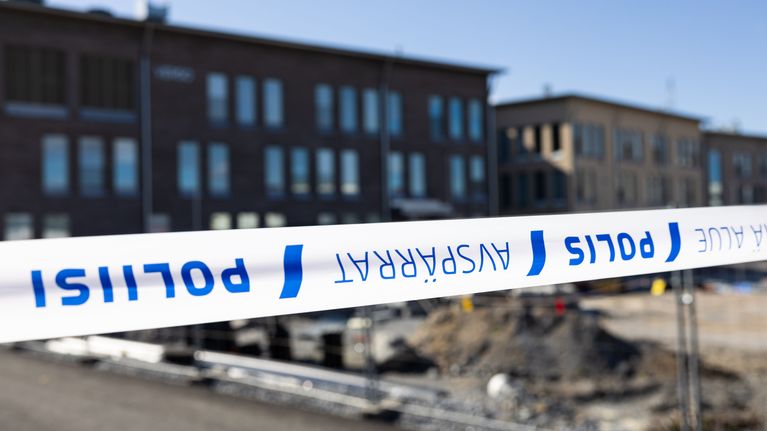 Vähäjärven valkotiilinen koulurakennus suorakaiteisine ikkunoineen aurinkoisena kesäpäivänä. Etualalla poliisin asettama valkosininen nauha.