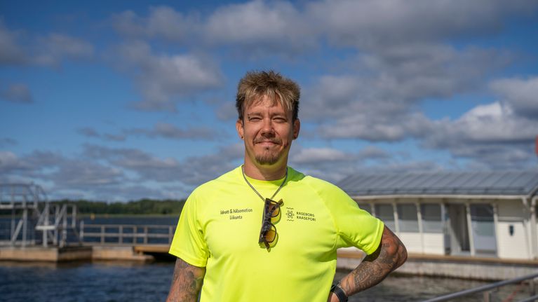 Man med neongul t-skjorta ler mot kameran på en badbrygga.
