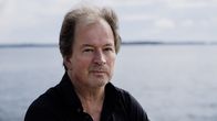 Kjell Westö lähikuvassa, taustalla merimaisema , katsoo vakavana kameraan.