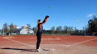 Pesäpallokentällä yksittäinen pelaaja harjoittelee pallon heittoa kirkkaassa kevätauringossa.