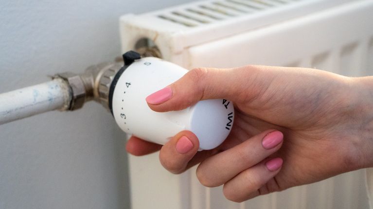 Käsi säätää lämpöpatterin termostaattia.