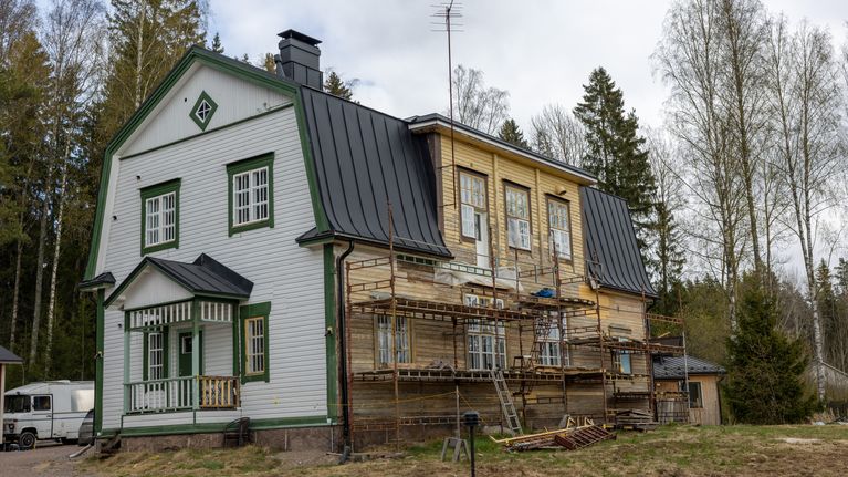 Skolhuset har två olika fasader, ena vit och grönmålad och en sida har byggställningar och är omålad. 