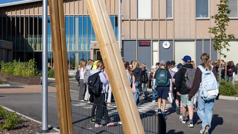 useita koululaisia kävelee kohti koulurakennusta reput selässään.