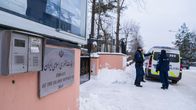 Tre poliser står vid en polisbil och en port vid en snöig gata.