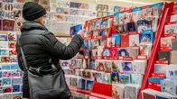 Nainen katselee joulukortteja kirjakaupassa hengityssuojain kasvoillaan.