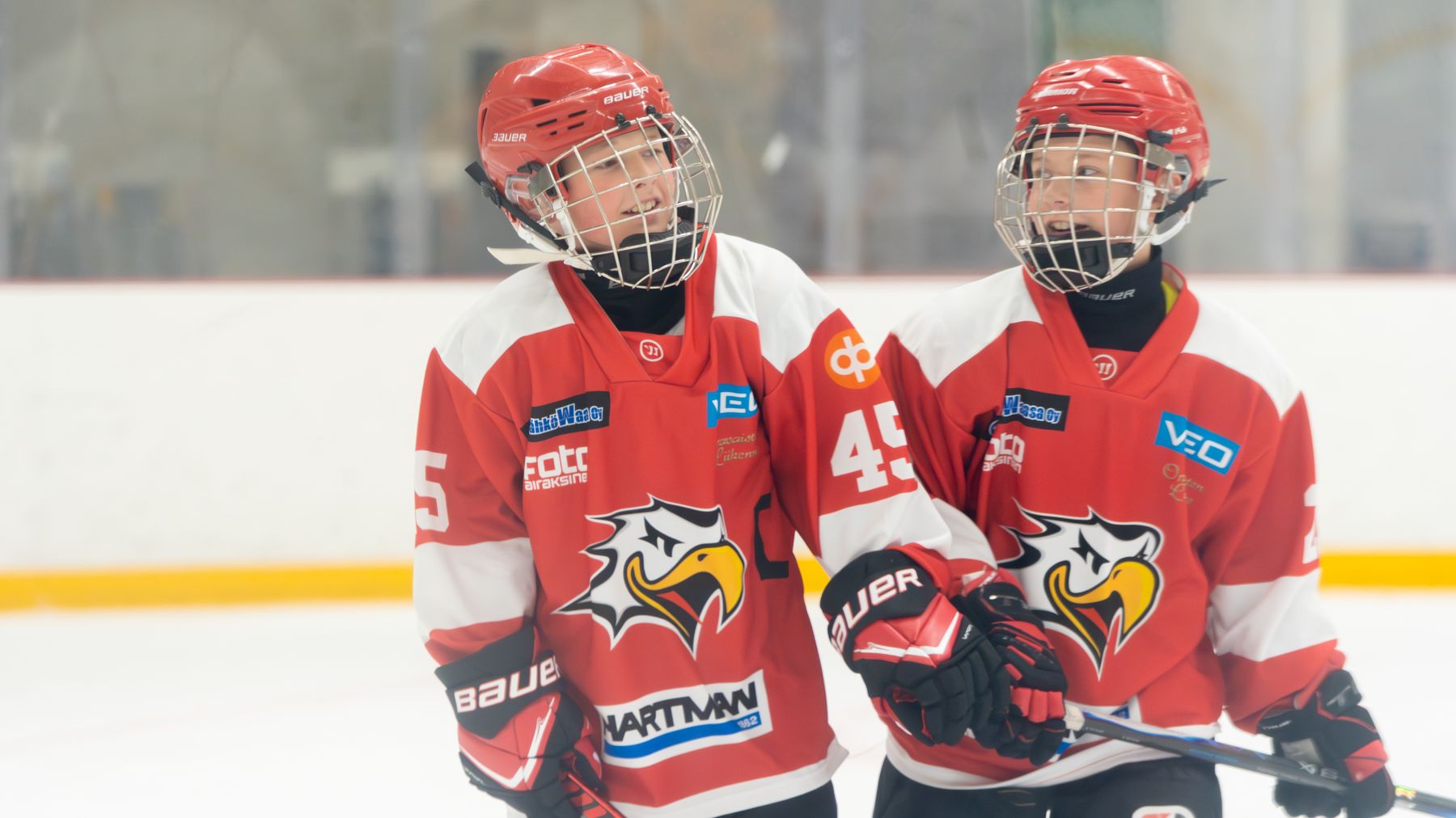 Två hockeyspelare i röda och vita dräkter står bredvid varandra på isen. 