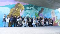 Flera ungdomar framför en färgglad muralmålning i en underfart.