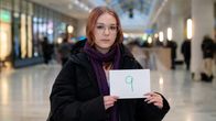 Nainen kauppakeskuksessa näyttämässä kirjoittamaansa arvosanaa paperilla.