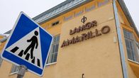 Ett gult stenhus i bakgrunden. I förgrunden ett trafikmärke för övergångsställe.