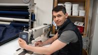 En ung man med mörkt hår sitter vid en industrisymaskin.