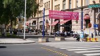 Ett stort övergångsställe framför en skylt där det står sommargågata. På gågatan sitter människor på uteserveringar.