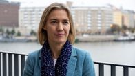 Amanda Sloat, klädd i turkos kavaj och blå halsduk, i halvnärbild medan hon tittar till vänster förbi kameran. 