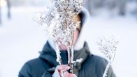 En anonym person, iklädd en grön vinterrock, håller en frusen grej framför sitt ansikte. Det är snö i bakgrunden.