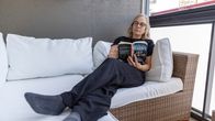 Oululainen Ritva Honka kerrostaloasuntonsa parvekkeella lukemassa kirjaa.