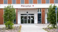 Rakennuksen sisäänkäynti, jonka yläpuolella on teksti "Päivystys" ja punainen risti, edessä kävelytie sekä kaksi puuta.