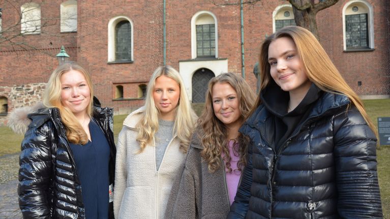 Fyra unga kvinnor klädda ler mot kameran. I bakgrunden syns Åbo domkyrka.