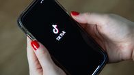 Photo shows a person holding a phone with the TikTok app open on the screen.