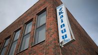 Tiilisen hotellirakennuksen kulmassa on pystysuora, alakulmasta särkynyt valokyltti, jossa lukee "Hotelli Kainuu"
